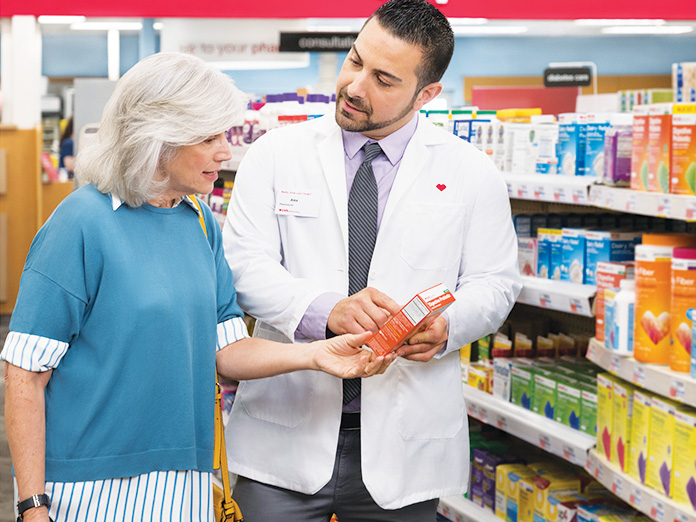 Imagen de un farmacéutico ayudando a una señora mayor a elegir un medicamento con receta en el pasillo de una tienda CVS