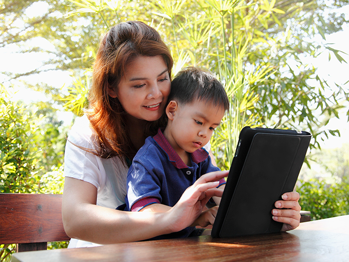 Madre e hijo usando una tableta sobre una mesa en el patio